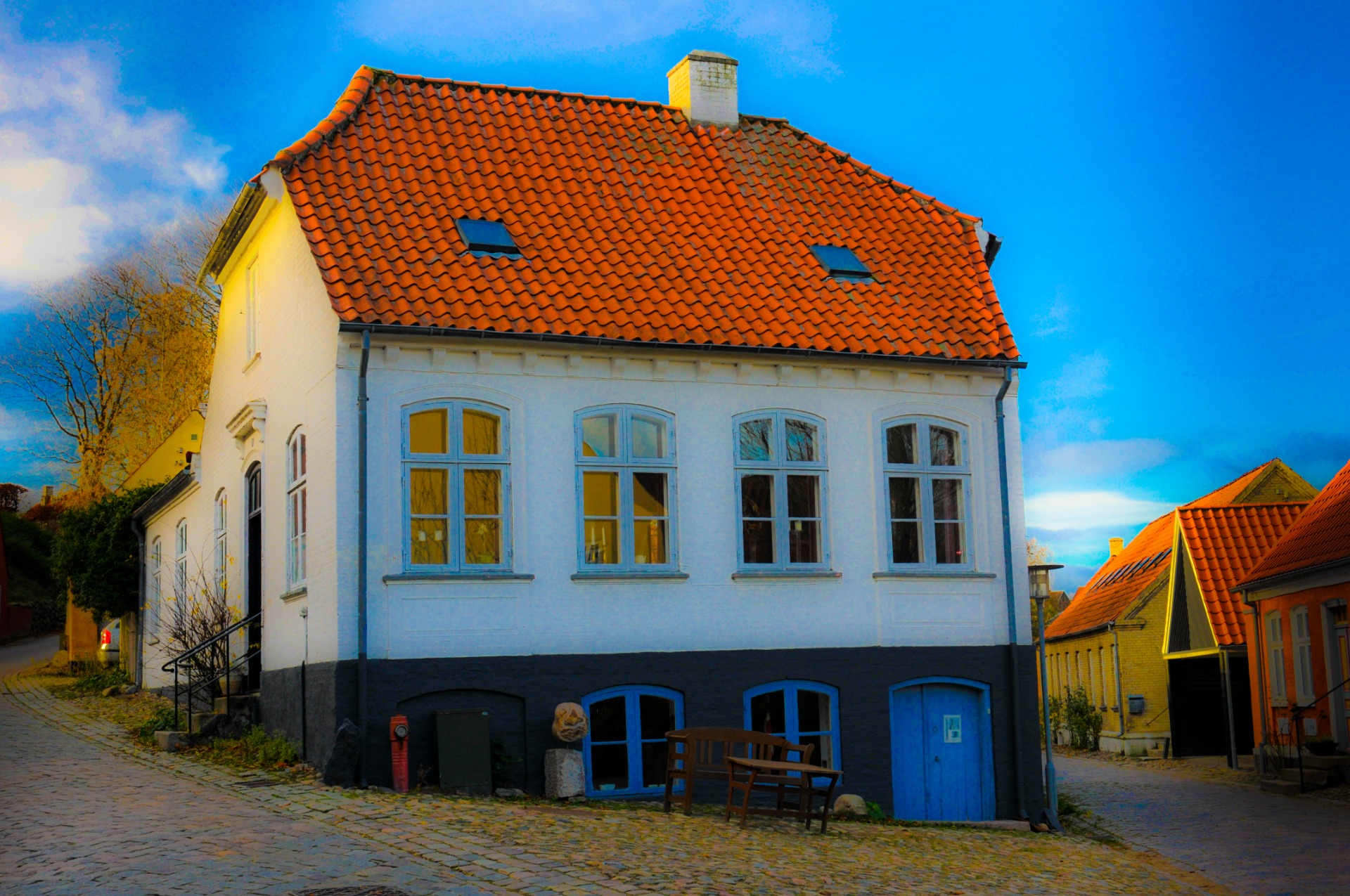 Hvidt hus med rødt tegltag, blå vinduesrammer og kviste mod klar blå himmel.